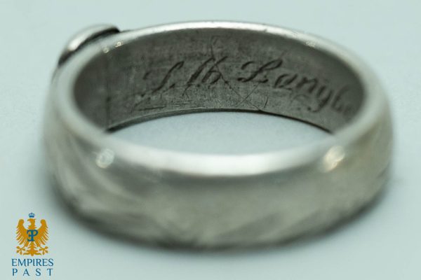 Close-up of a silver signet ring with a blurred cursive inscription along the inner band; Empires Past logo visible in the bottom-left corner.