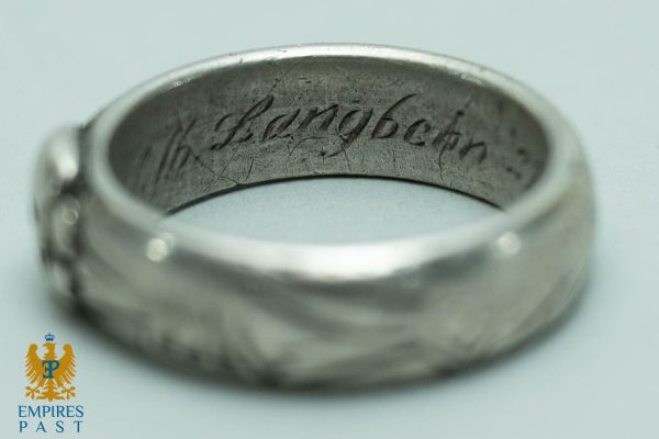 Close-up of the inner band of a silver ring with a cursive inscription. The surface is scratched and worn as in a vintage piece.