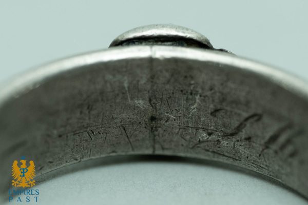 Close-up of a scratched, curved metal band with a small knob on top, set against a pale blue background; Empires Past logo bottom-left.
