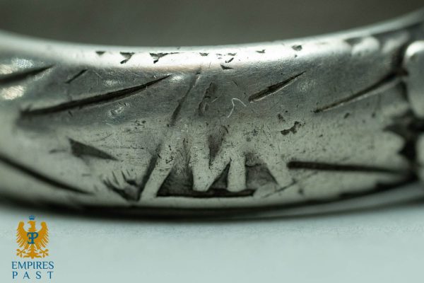 Close-up of a worn silver ring with abstract engraving and scratches; Empire's Past logo appears in the bottom-left corner.