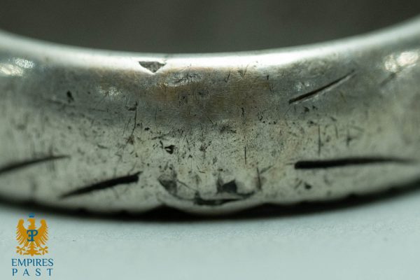 Macro close-up of a scratched, worn metal edge, likely an artifact, with the Empires Past watermark in the lower-left corner.