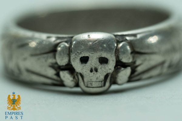 Close-up of a weathered silver skull ring, with a prominent skull centerpiece and band rings; Empires Past logo in the corner.