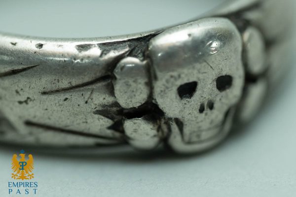 Close-up of a worn silver ring with scratches and dents, showing a rugged, aged texture. Empires Past logo visible in the corner.