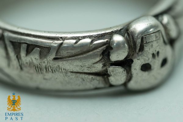 Close-up of a carved silver ring showing a textured leaf pattern and worn edges; Empire's Past logo visible in the lower left.