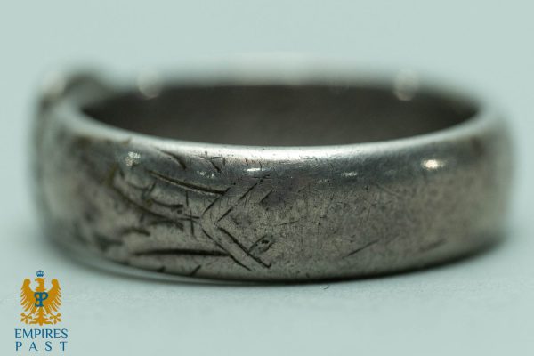 Close-up of a worn silver ring with numerous scratches and etched lines, showing heavy wear.