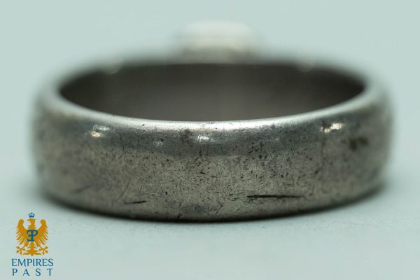 Close-up of a worn silver ring with numerous scratches, resting on a light surface; Empire Past logo appears in the bottom-left corner.
