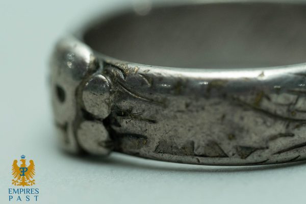 Close-up of a tarnished metal ring with grime and scratches; Empires Past logo visible in the bottom-left corner.