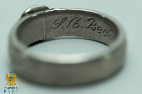 Close-up of a silver ring with an engraved script inside, reading 'H.G. Berg'.
