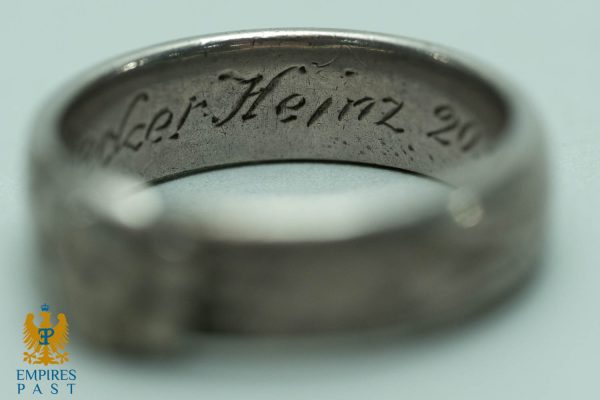 Macro close-up of a silver ring showing an engraved cursive inscription along the inner band (text partially legible).