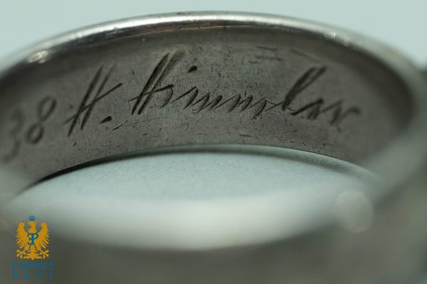 Close-up of a silver ring with an engraved cursive inscription; Empires Past logo in bottom-left corner.